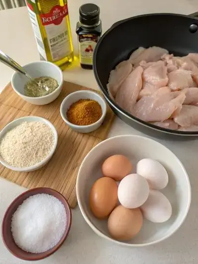 Raw chicken tender and seasonings arranged on a kitchen table.