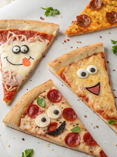 Pizza slices decorated with cheese, pepperoni, and toppings arranged like silly faces.